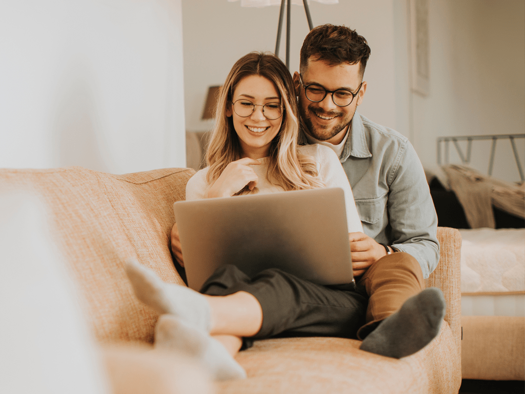 Young Couple on Sofa Smiling at Laptop