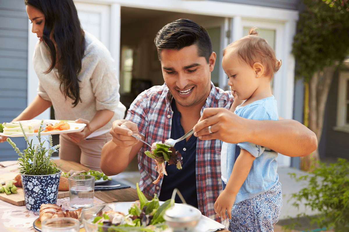 Smiling father serving summer salad to his infant child
